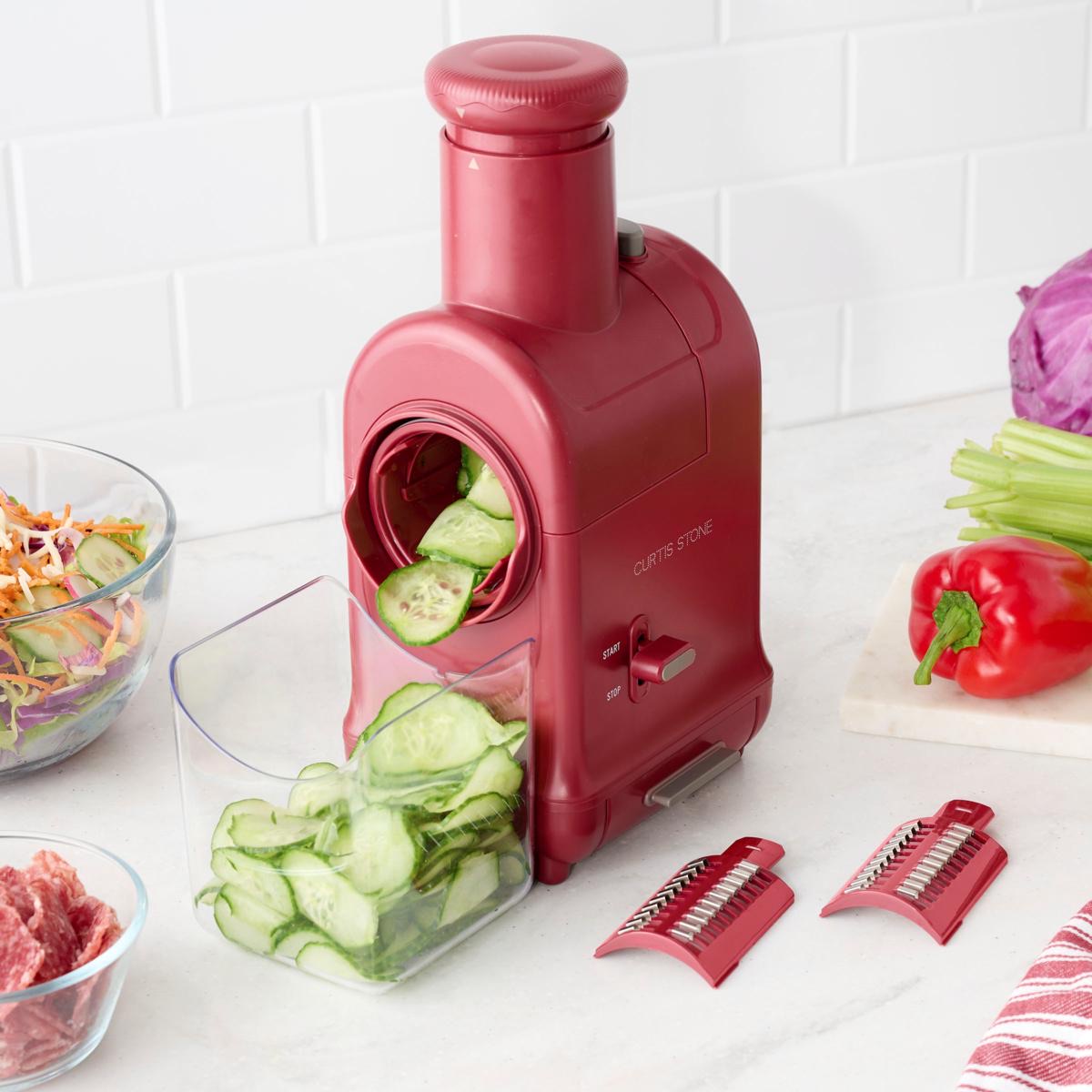 Curtis Stone Electric Prep Master Slicer on a kitchen counter with the blade storage drawer open and two drums beside it